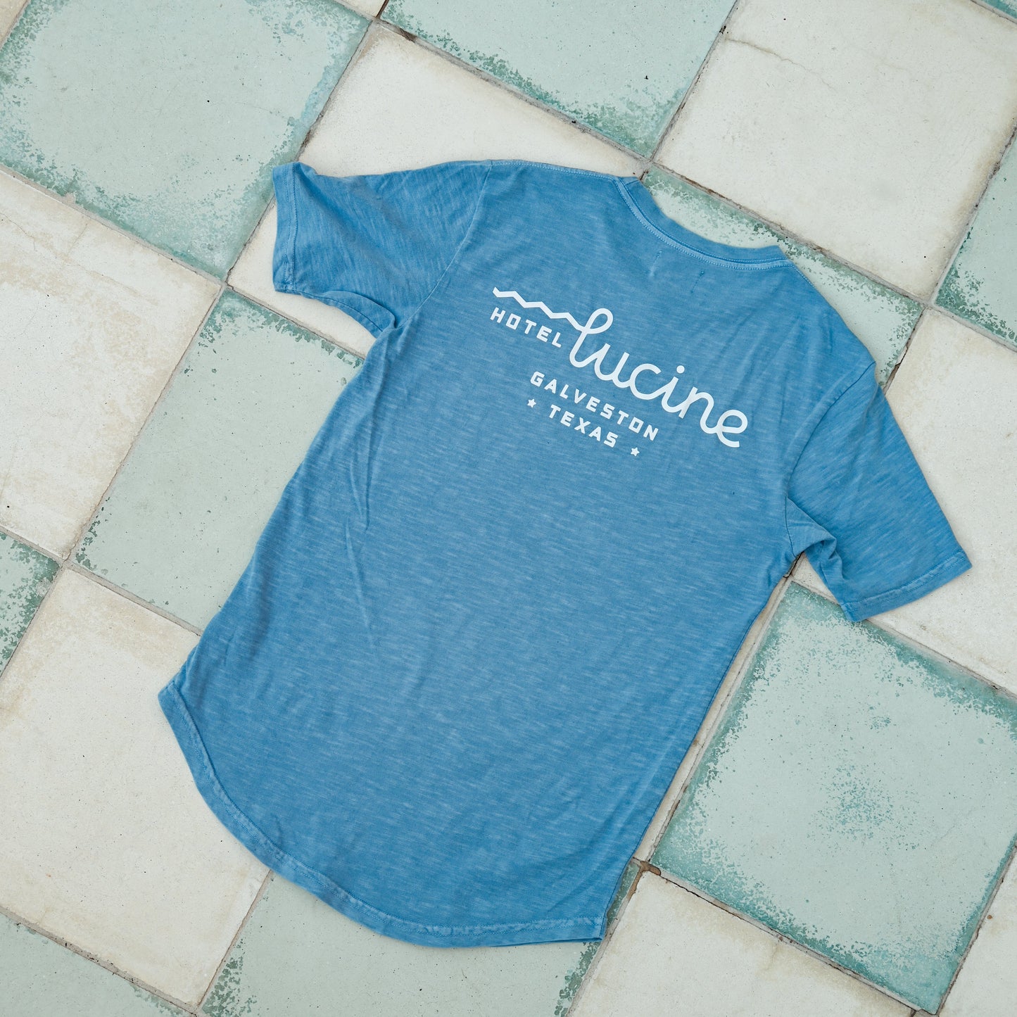 Blue t-shirt with 'Hotel Lucine' text on a tiled floor